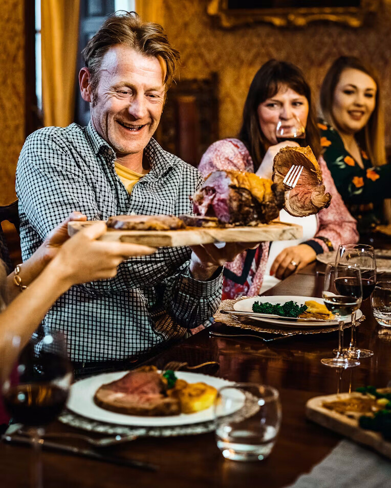 A roast passed across a long dinner table